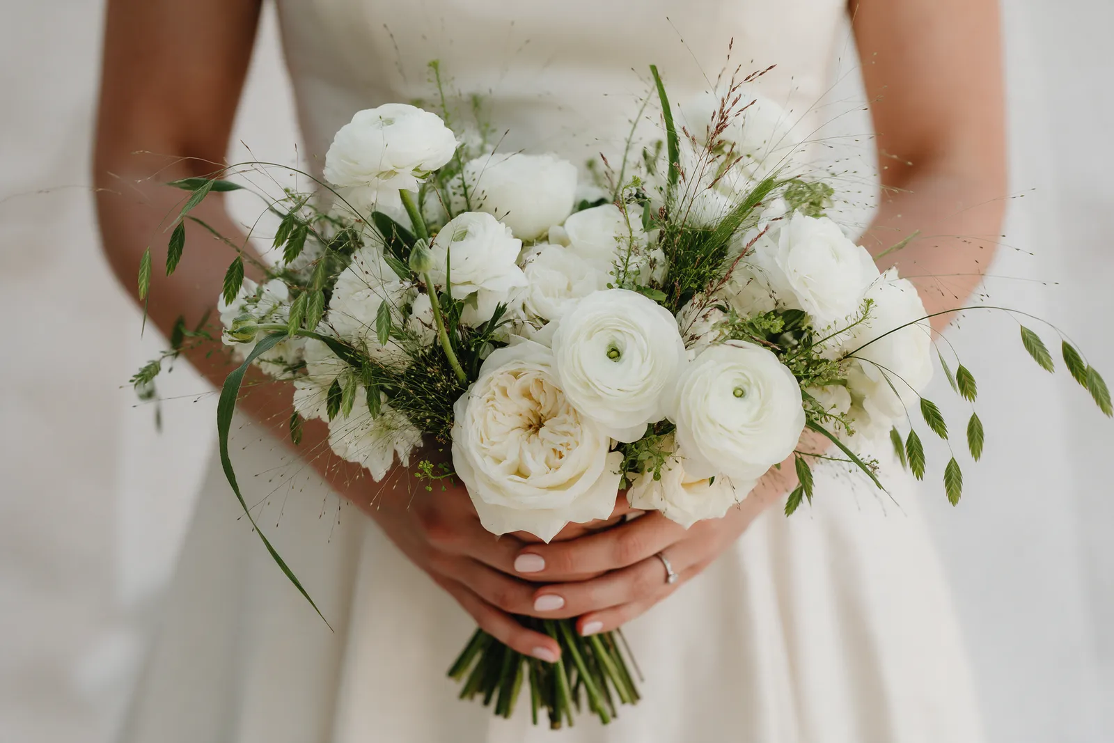 A loose bridal bouquet of white ranunculus and garden roses