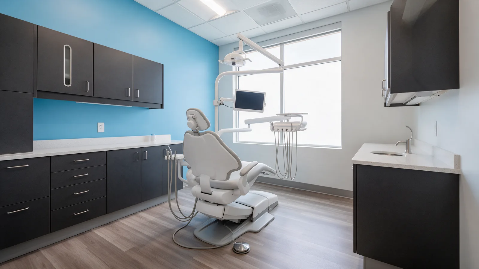 A bright modern dental surgery: a white dental chair, a sky-blue feature wall, charcoal cabinetry and a large window