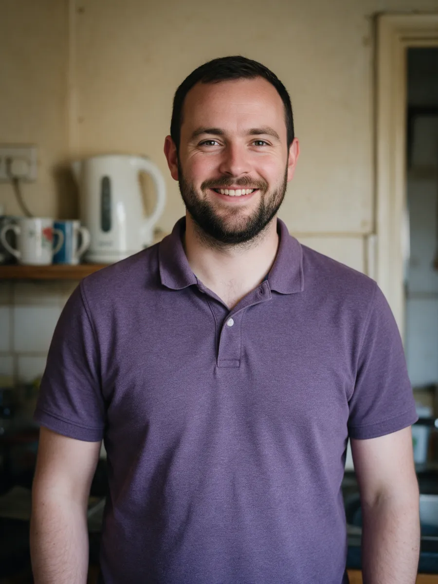 Tomos Bevan, a man in his thirties with a short dark beard in a heather polo shirt, smiling in the kitchen of a client's home