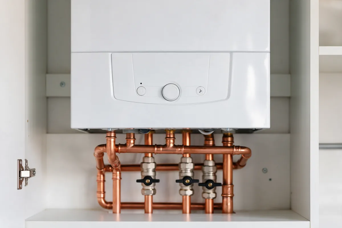 A newly installed white combi boiler with neat copper pipework in a kitchen cupboard
