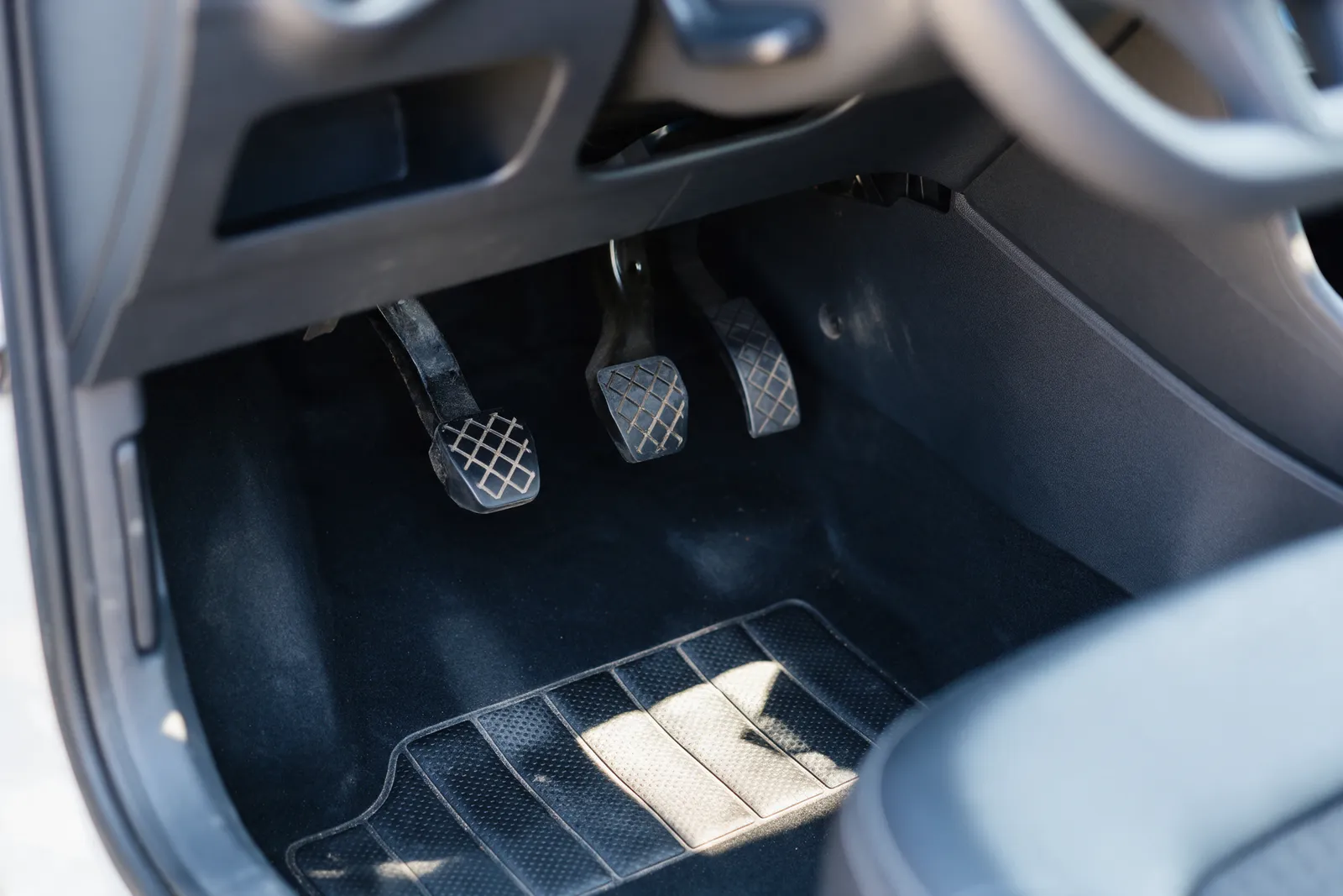 A close-up of the footwell of a driving-school car showing the instructor's dual control pedals