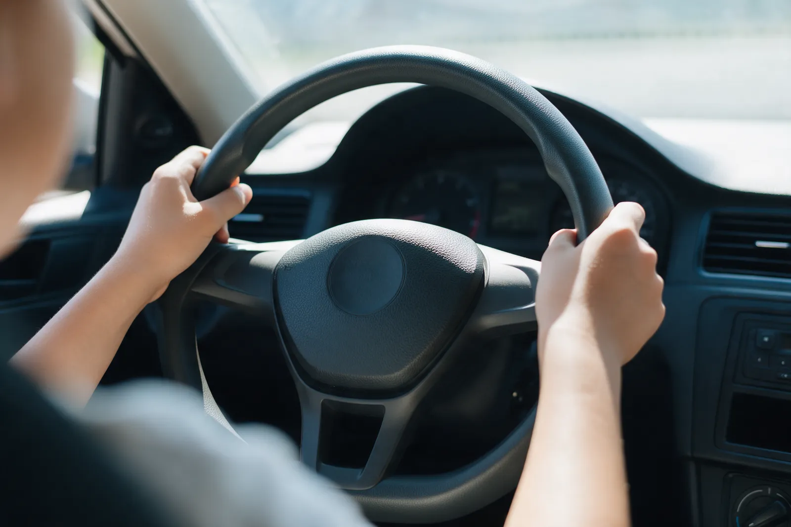 A close-up of a young learner's hands on a steering wheel at ten to two with bright daylight through the windscreen