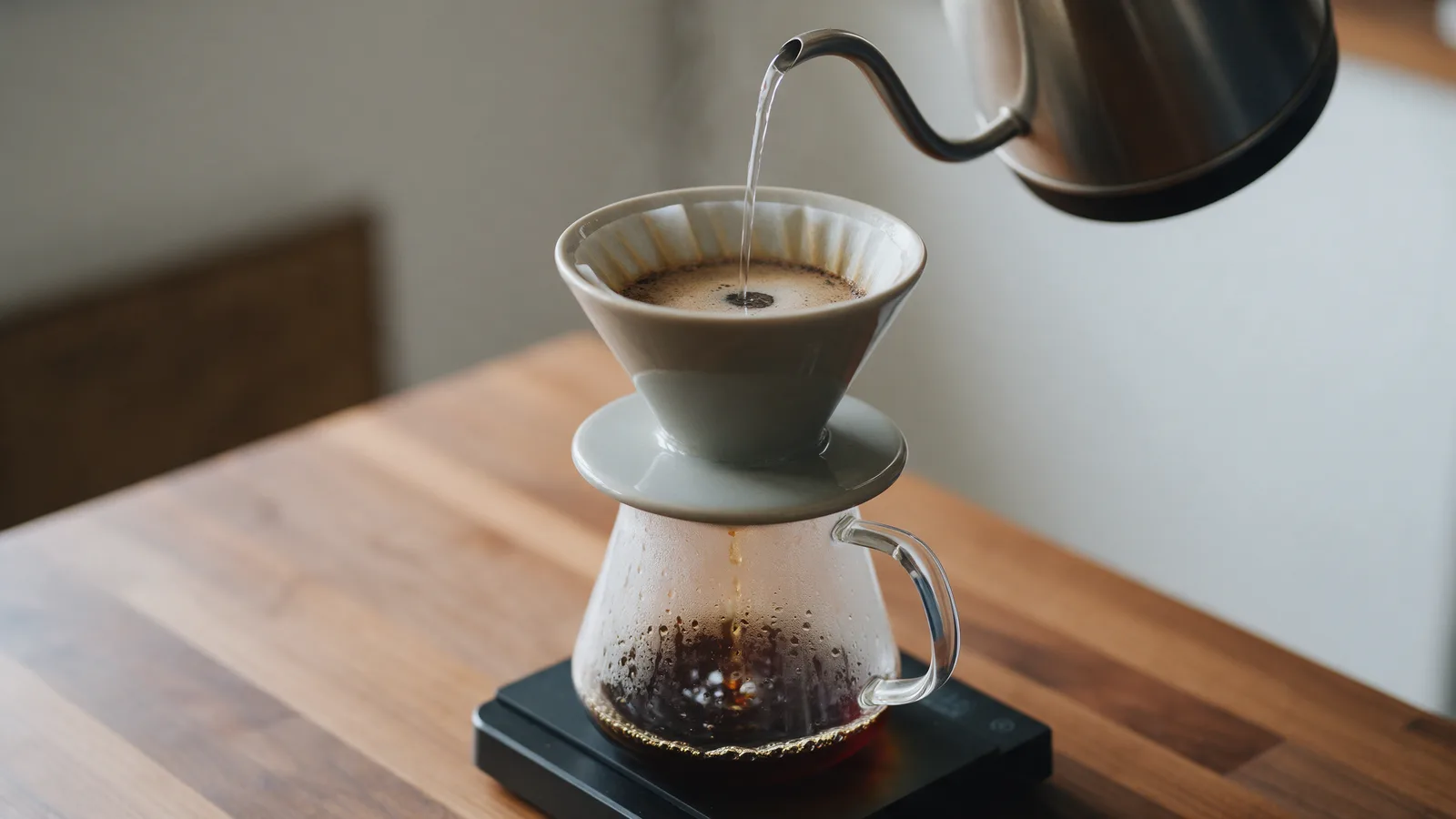 A gooseneck kettle pouring into a ceramic dripper on a scale