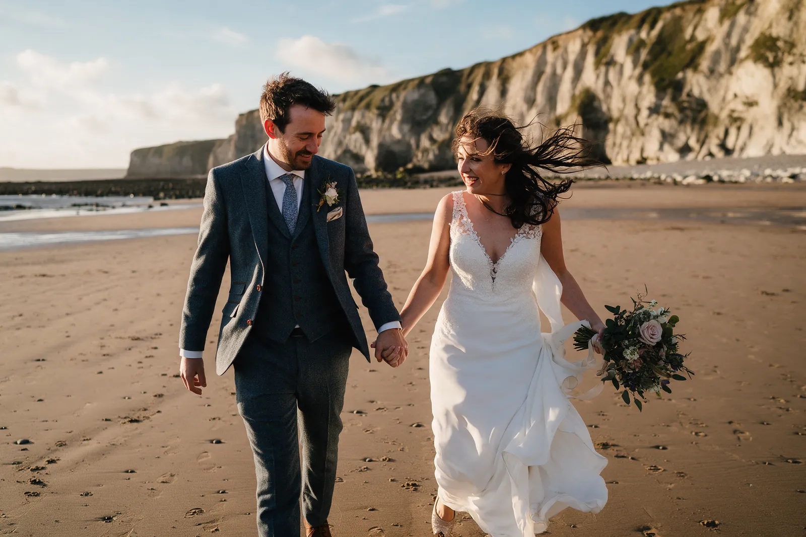 A couple on a wide sandy beach at low tide with cliffs behind