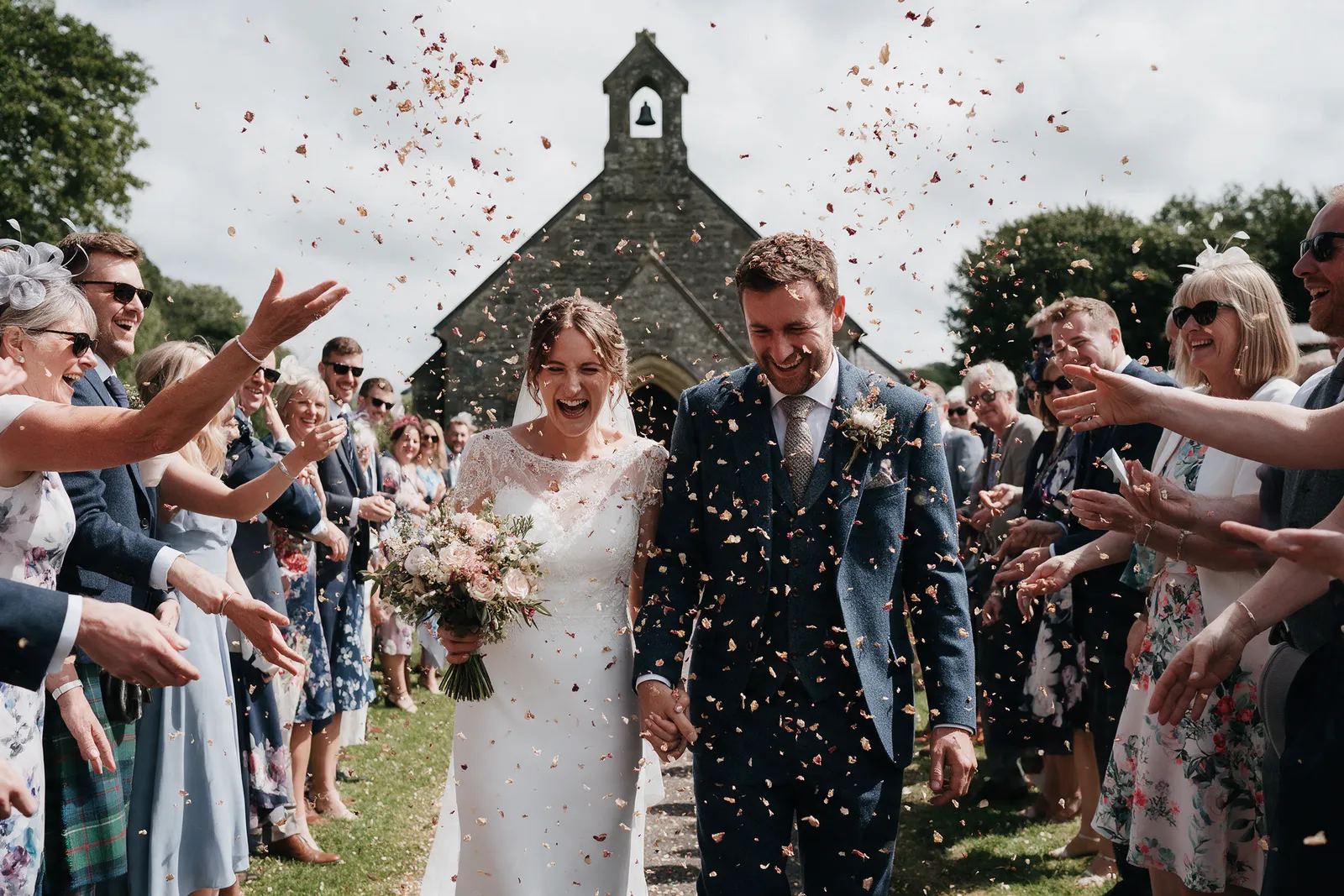 A couple walking through a confetti shower outside a stone church