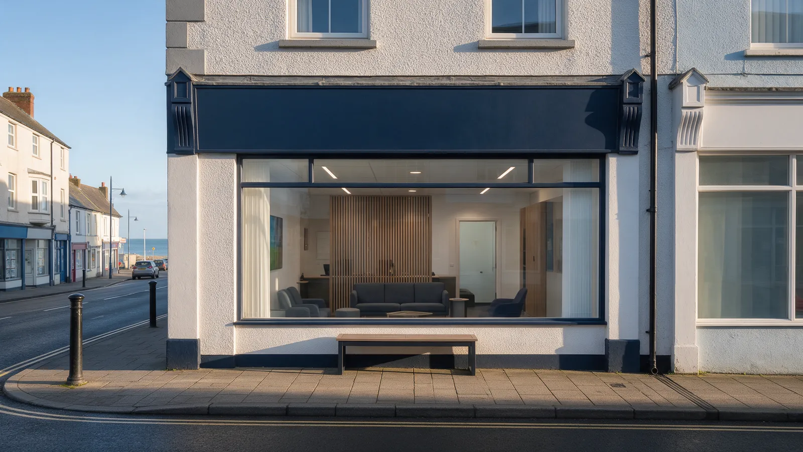 A solicitor's office front on a high street in a Welsh seaside town, a navy fascia, a large window with a modern lobby visible inside and a bench outside