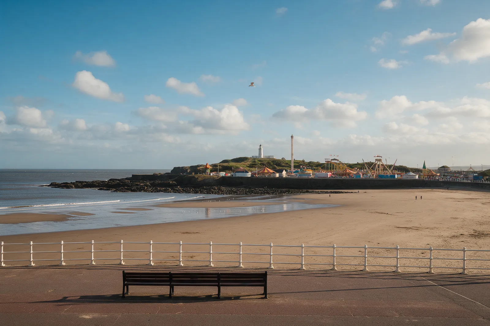 A seaside promenade with a wide sandy bay and a pleasure-park headland in the distance