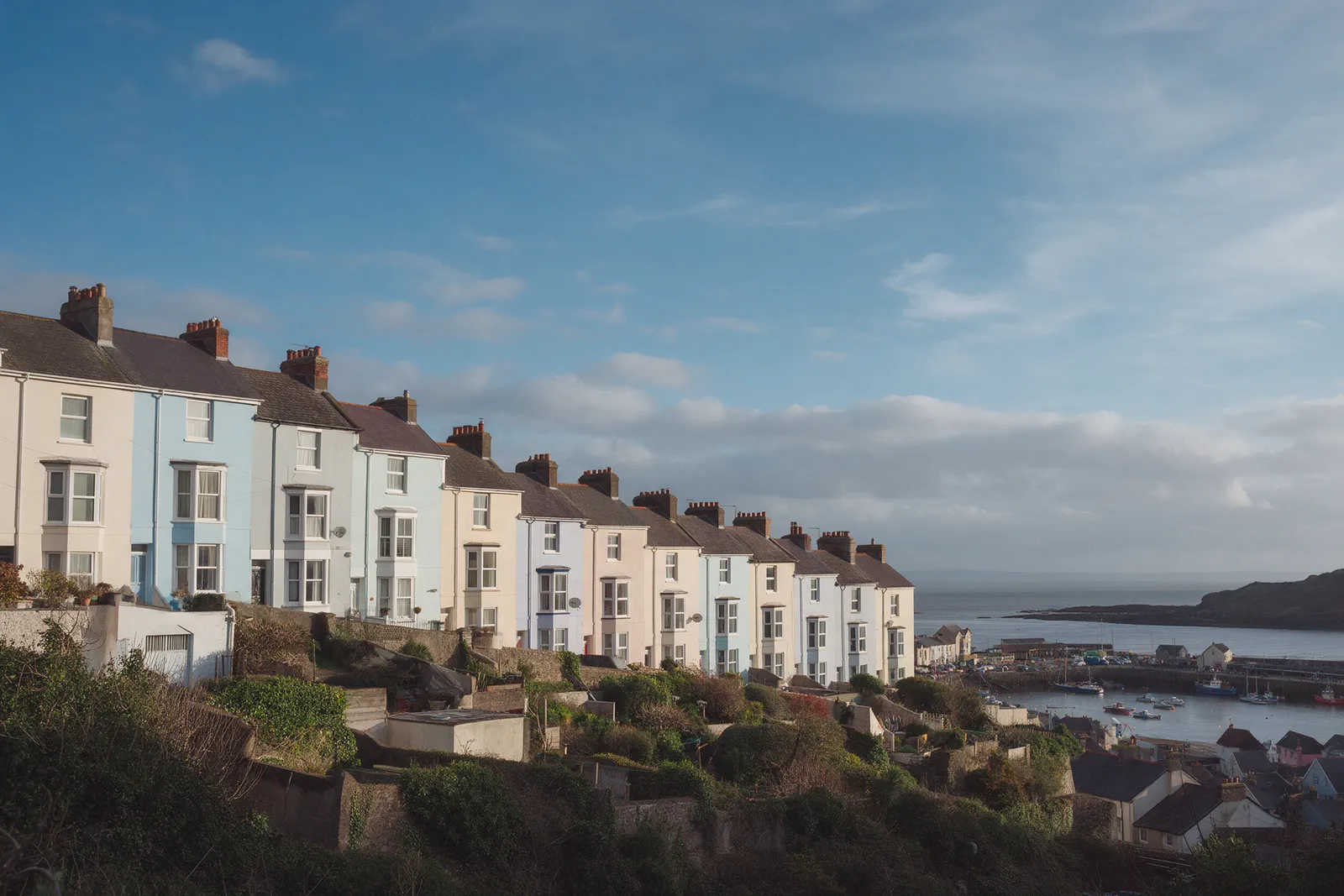 A row of pastel-painted Victorian terraced houses on a hill above a seaside harbour in South Wales