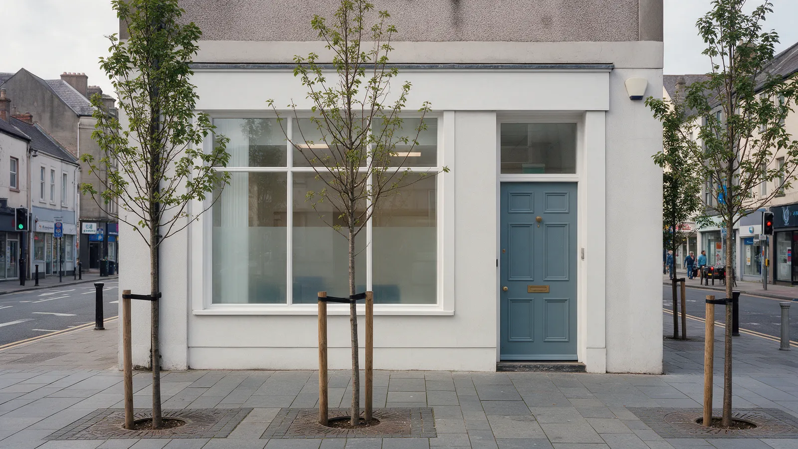A clinic frontage on a city street with a bluestone-grey door, large window and young trees planted along the pavement