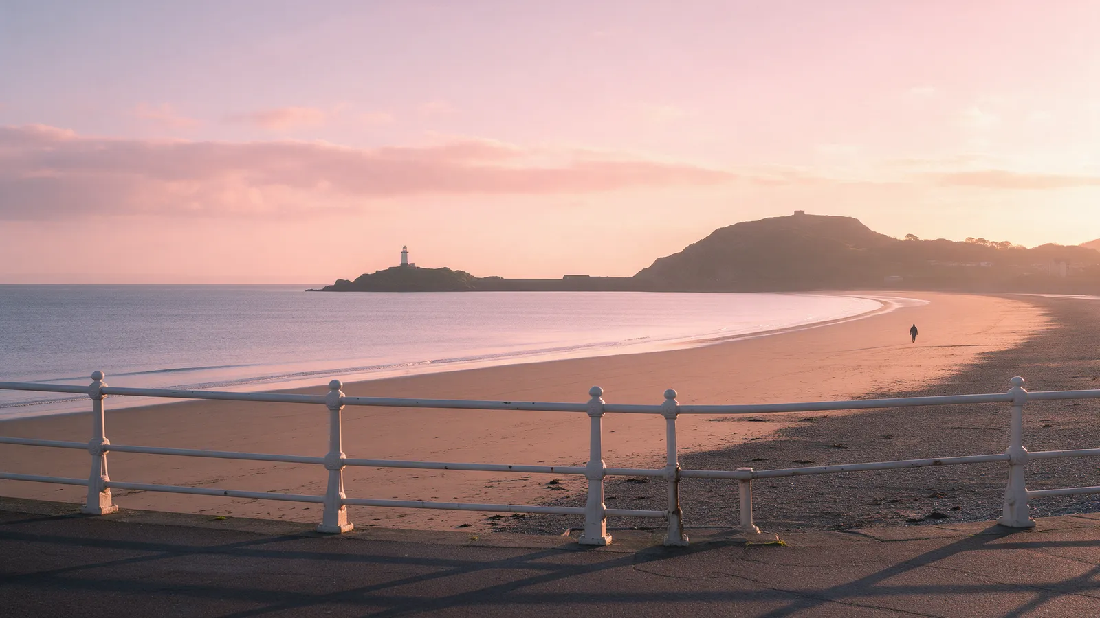 Swansea Bay at sunrise seen from the promenade, the long curve of sand and the Mumbles headland in soft light