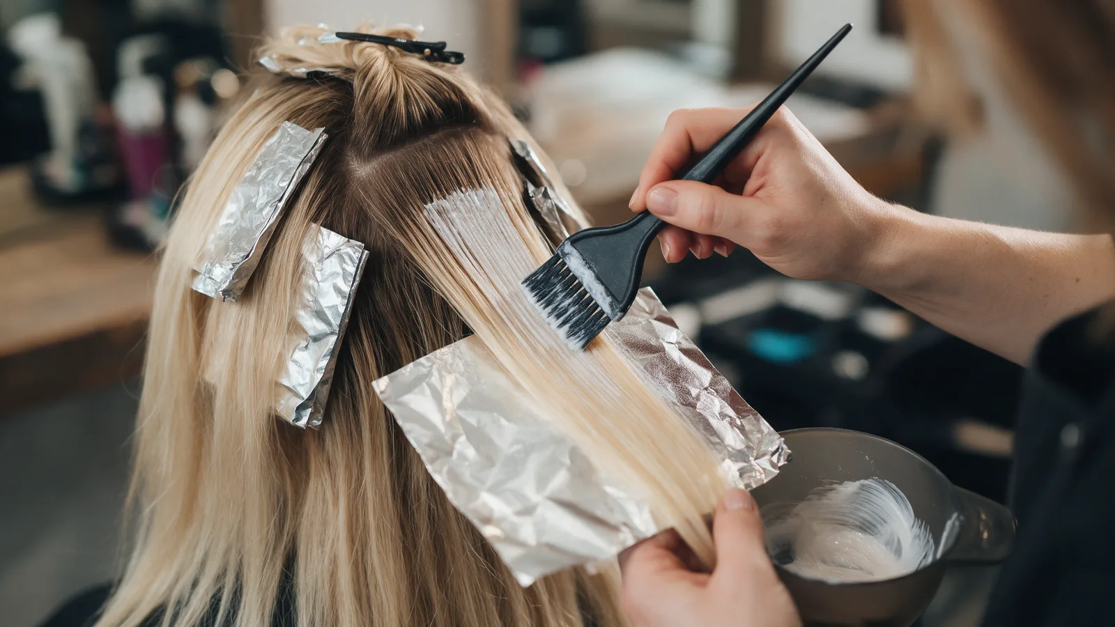A colourist painting balayage onto sections of long blonde hair with a brush and foils