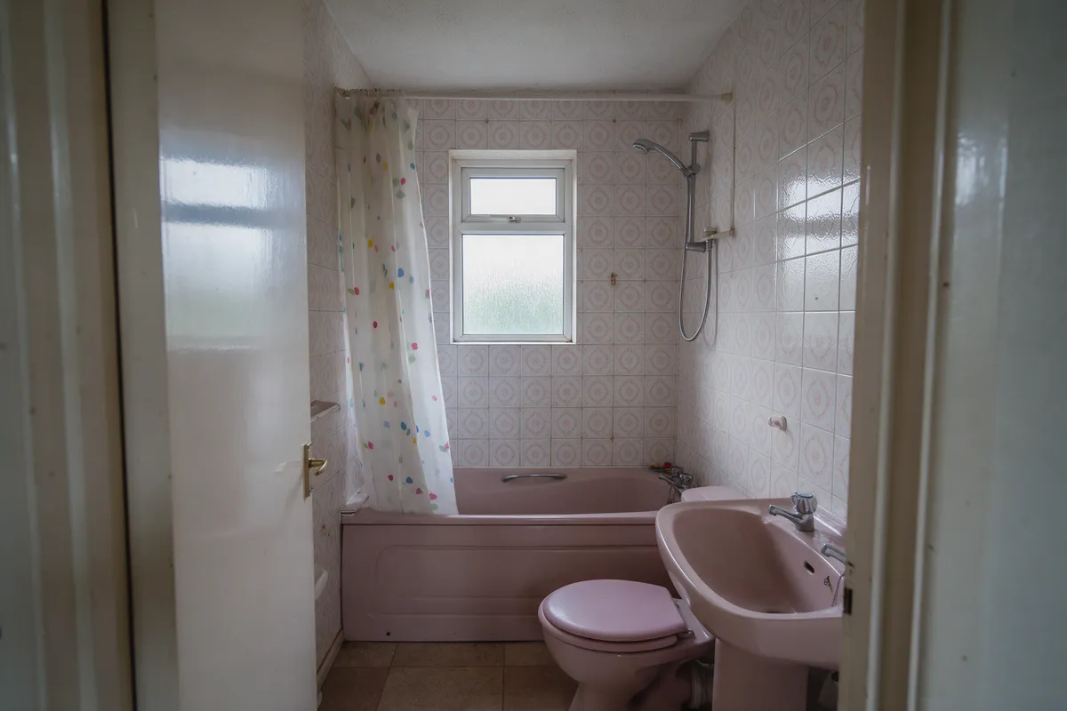 Before: a dated 1980s bathroom with a pink suite and patterned tiles