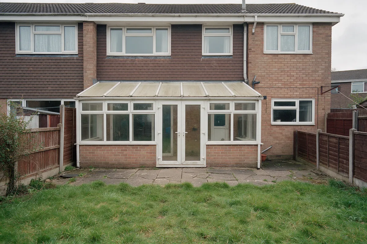 Before: the rear of a 1970s semi with a tired white conservatory and cracked patio