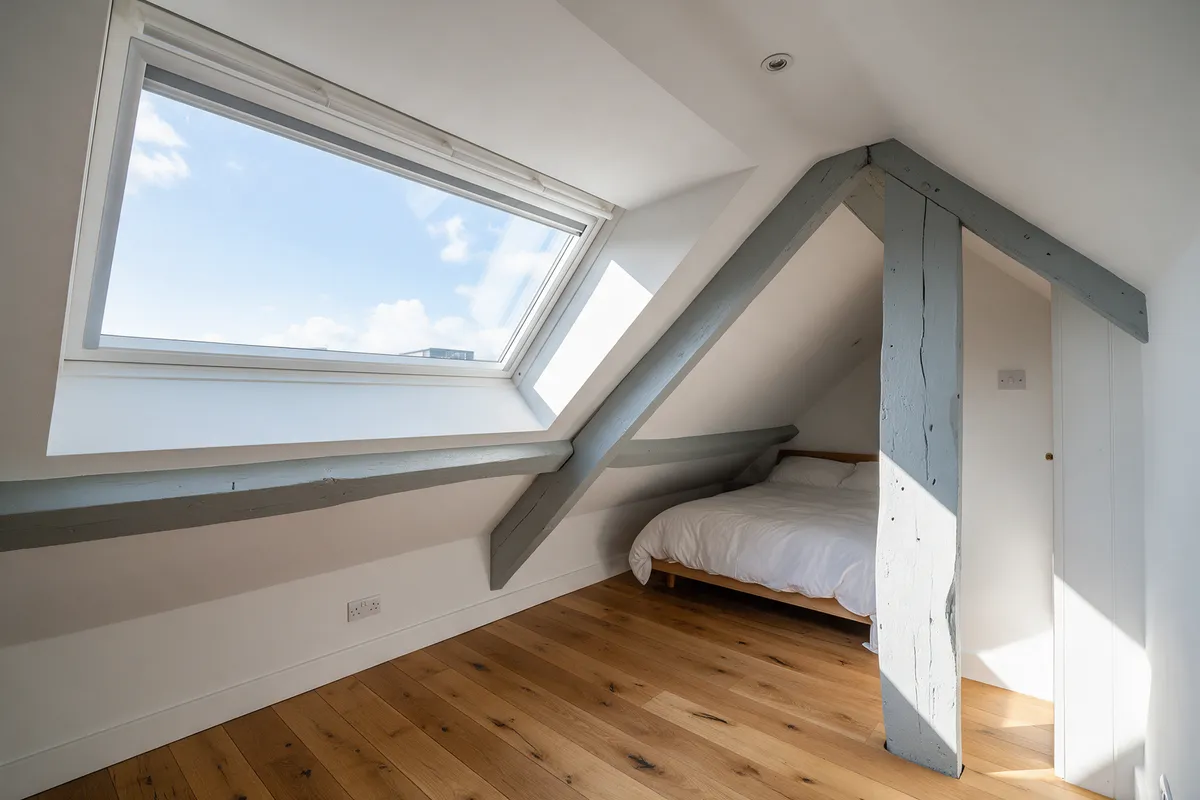 A loft bedroom with a large dormer window and oak floor