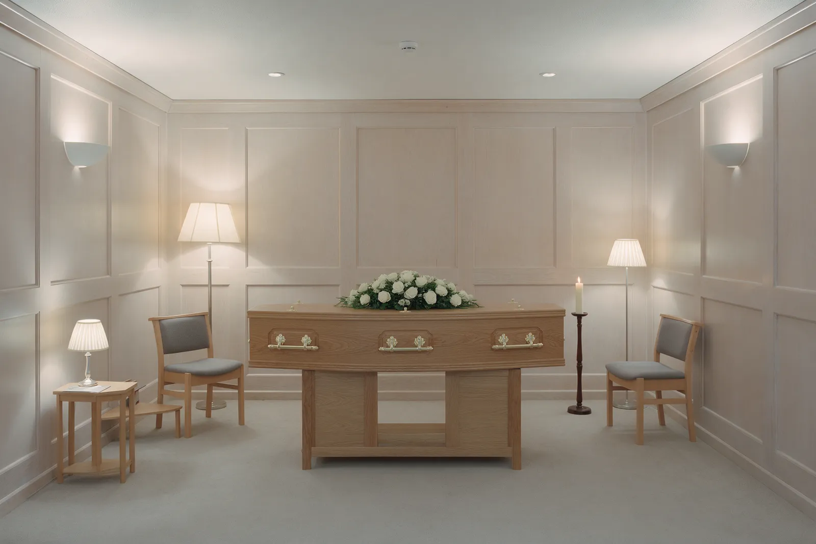 A quiet chapel of rest with pale wood panelling, a single candle, soft lamps, two chairs and a closed oak coffin with a spray of white roses