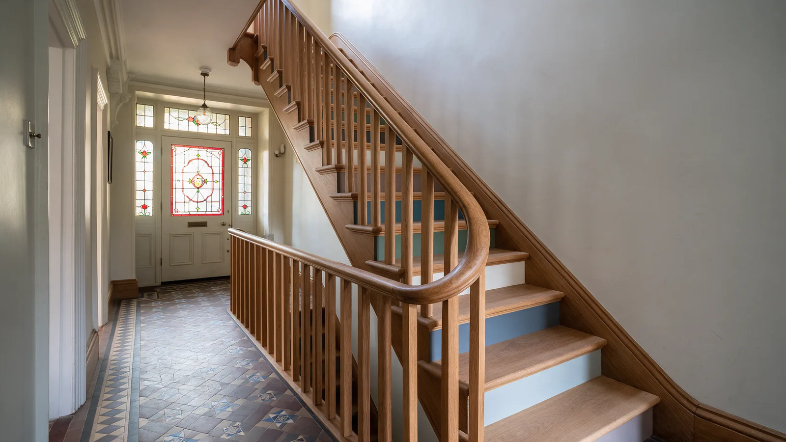 A new solid oak staircase with a curved handrail and square spindles in a period hallway with an encaustic tiled floor