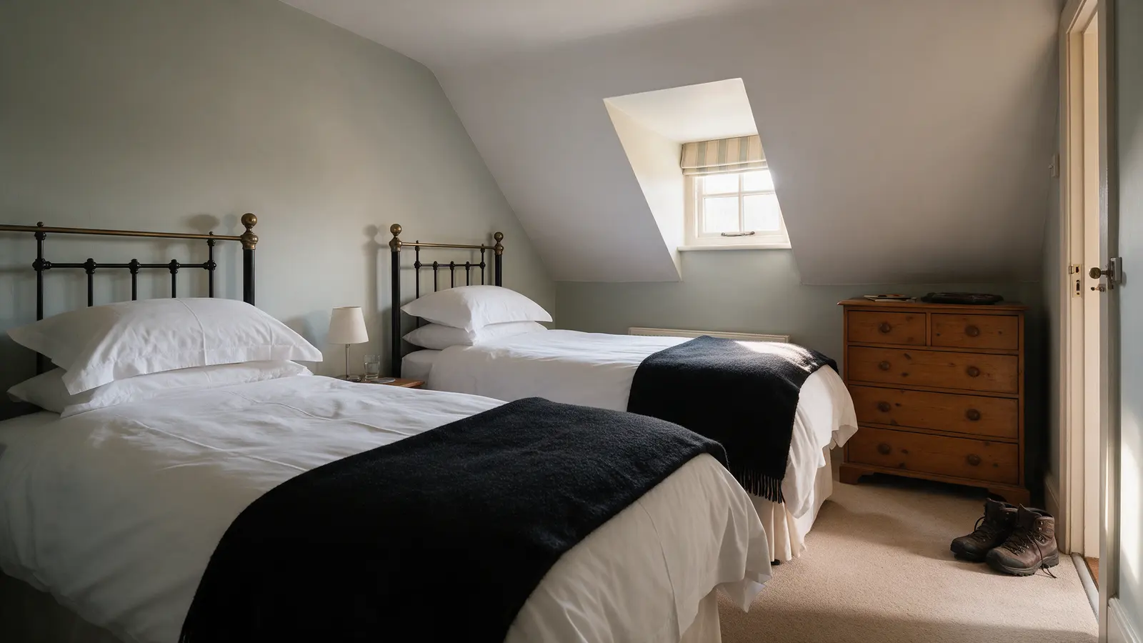 Penny Black: a twin room in the eaves with two single beds, black wool throws, a sloping ceiling with a dormer window and walking boots by the door