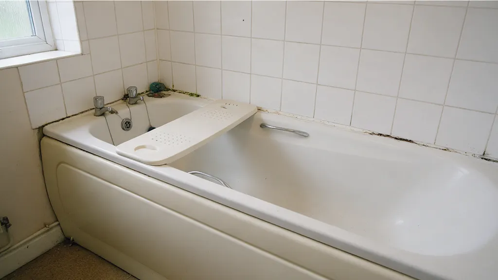 The same bathroom before: a 1990s suite with a high-sided bath, a bath board and mouldy sealant