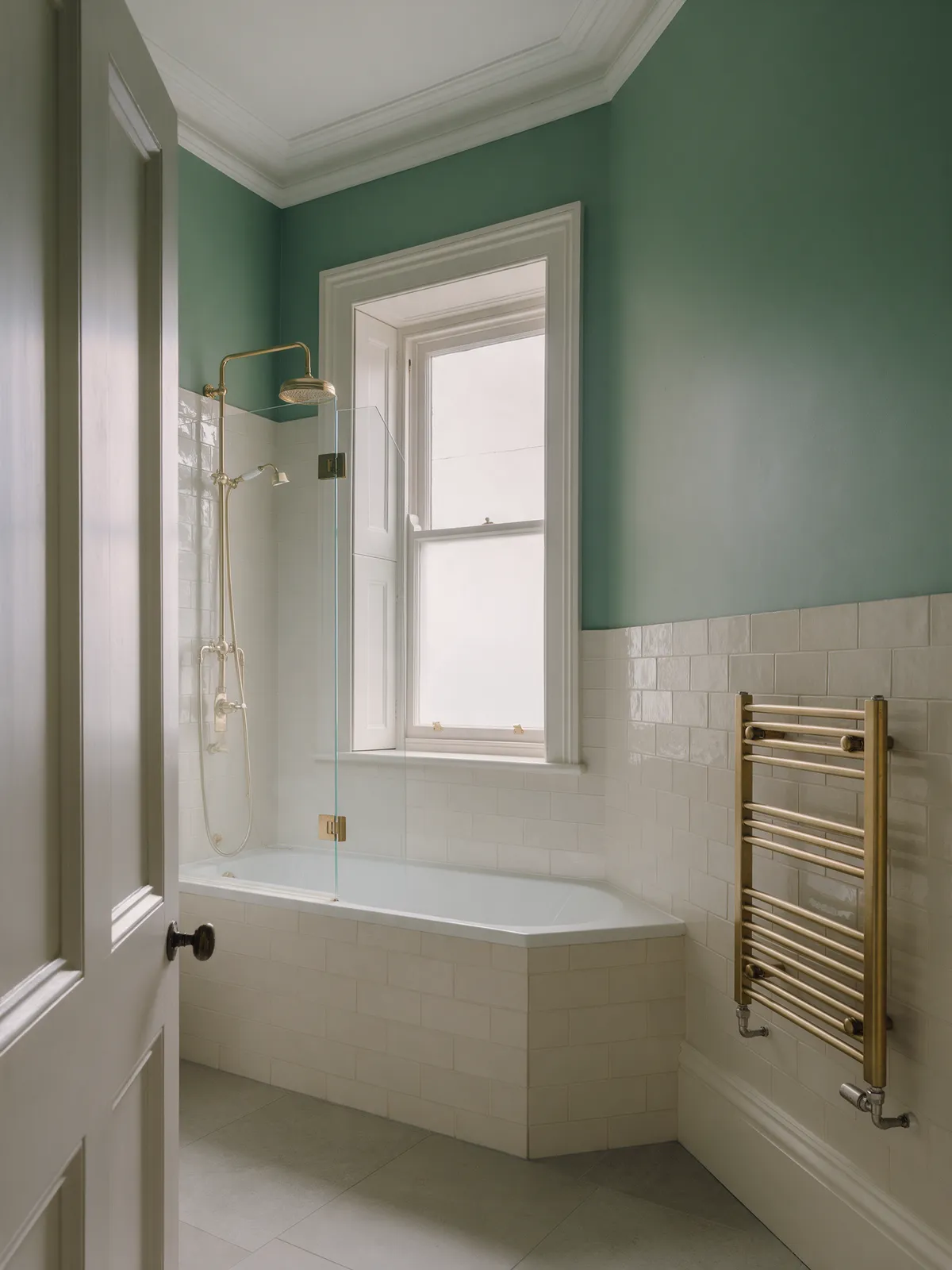 The finished bathroom with a thermostatic shower over the bath, a hinged glass screen and pale tiles