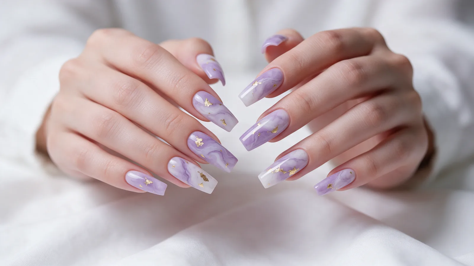 Two hands with long coffin-shaped nails in a lavender and white marble nail art with gold foil flecks