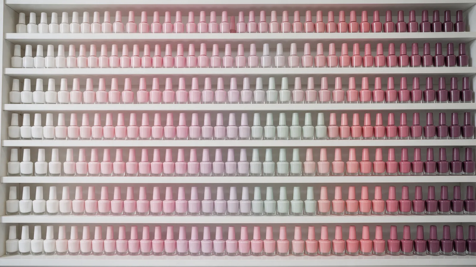 A wall of gel polish bottles arranged by colour from white through pinks, lavenders and mints to deep plum