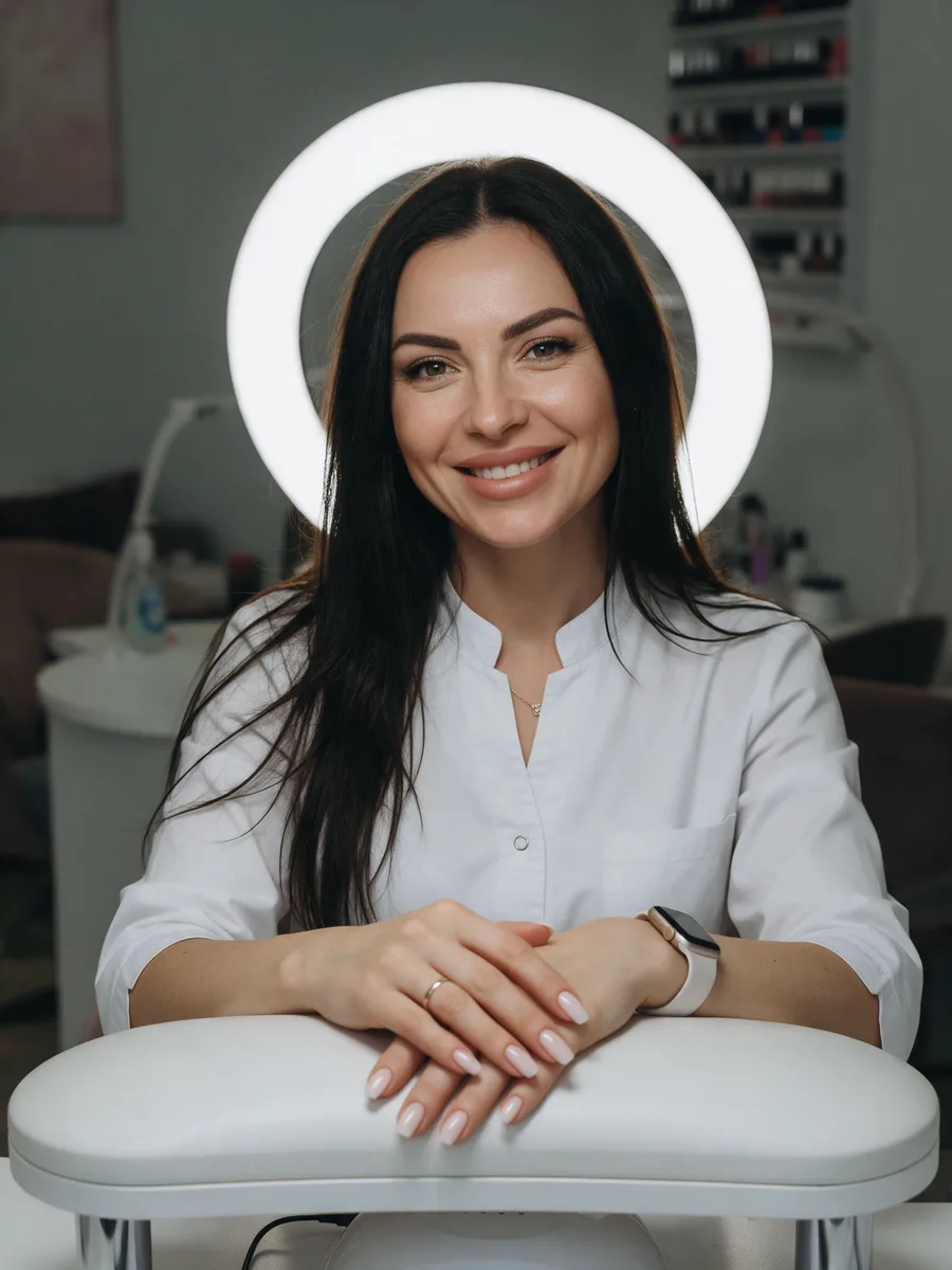 Siân Hughes sitting at a nail desk with a ring light, white tunic, manicured nails