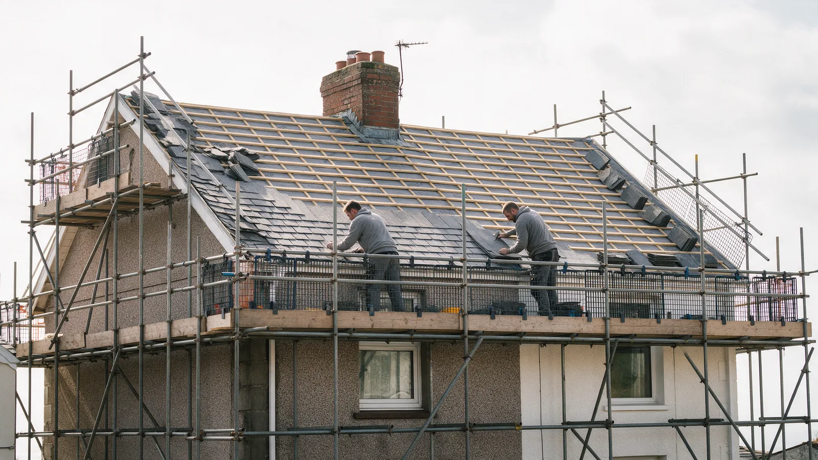 A terraced house roof mid re-roof with new membrane and battens and roofers laying slates from the eaves