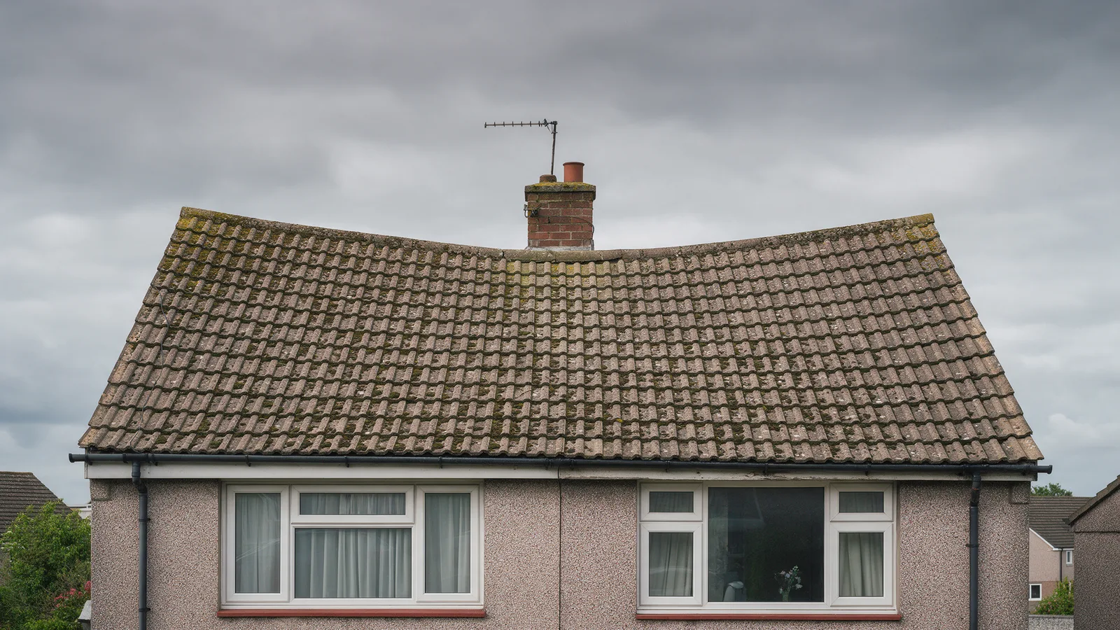 The same semi-detached house before: faded mossy concrete tiles, sagging ridge and cracked verges
