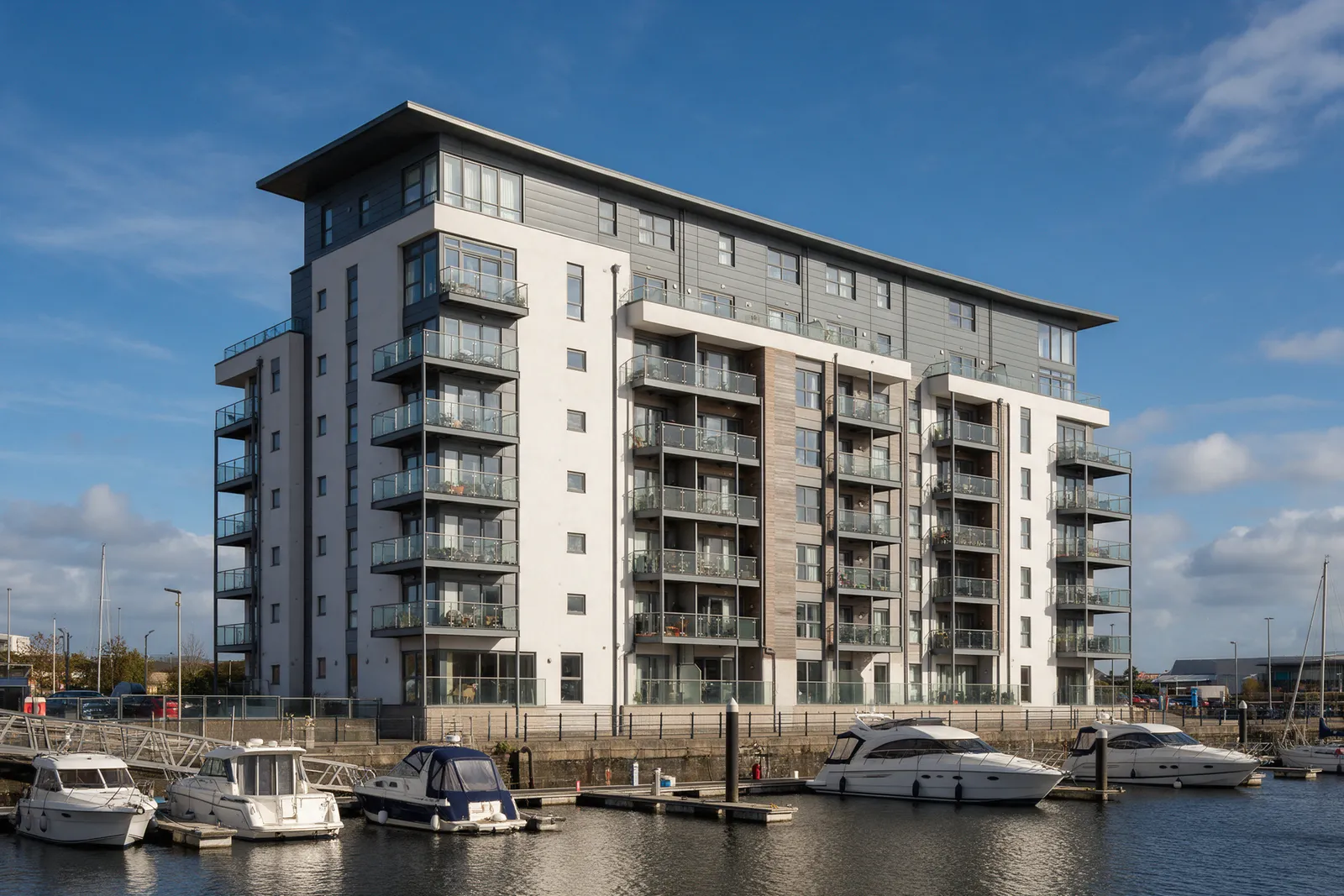 A modern waterfront apartment building with balconies overlooking a marina with yachts under a blue sky