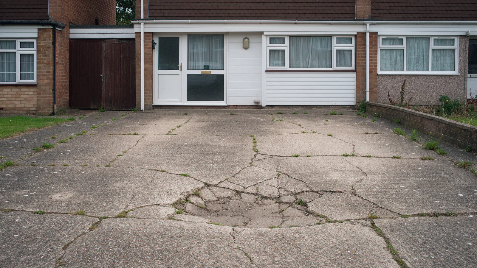 The driveway before: cracked and sunken concrete with weeds in the joints in front of a 1970s semi