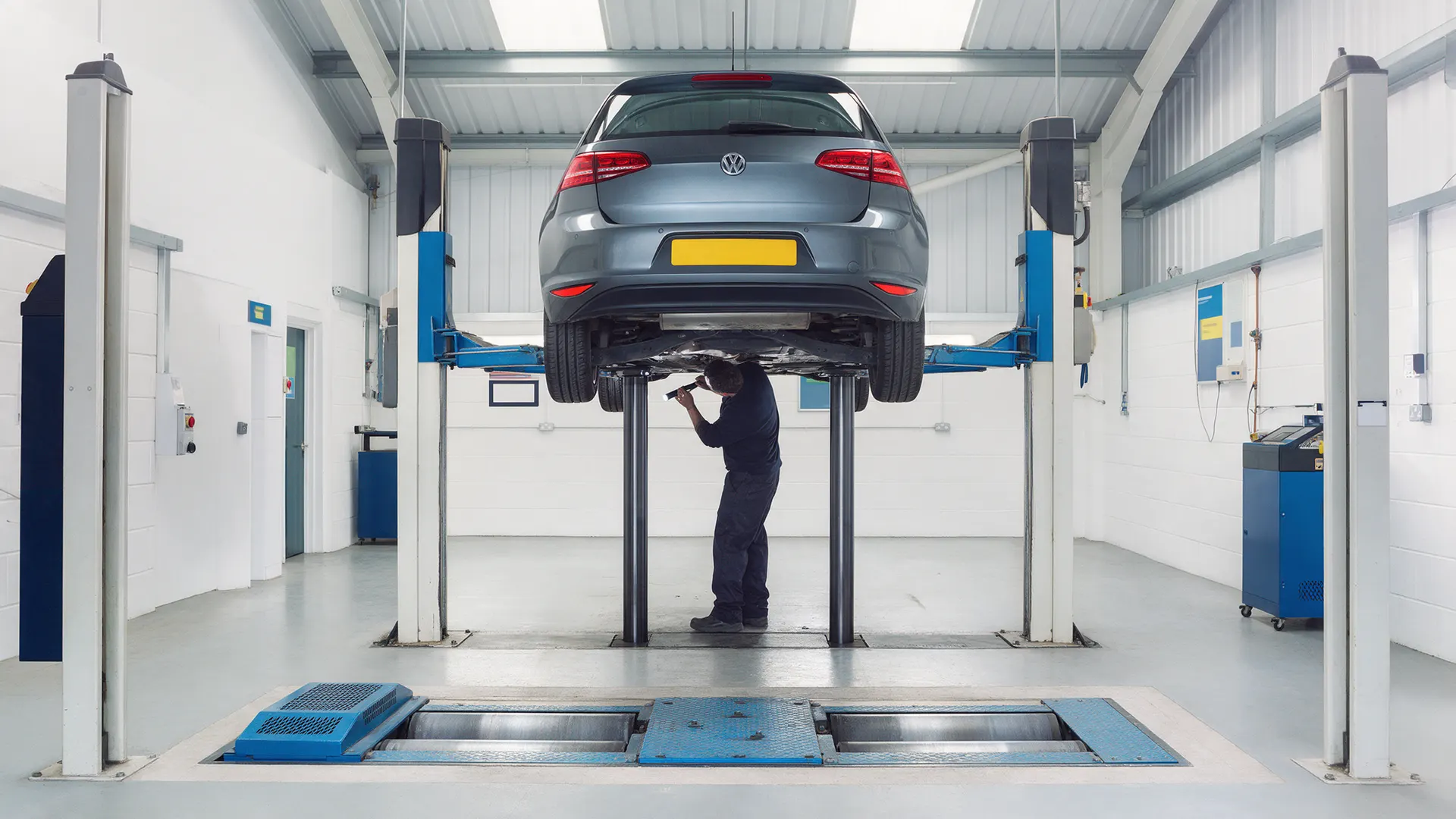 A hatchback raised on the lift in the Taff MOT Centre test bay with a tester checking underneath
