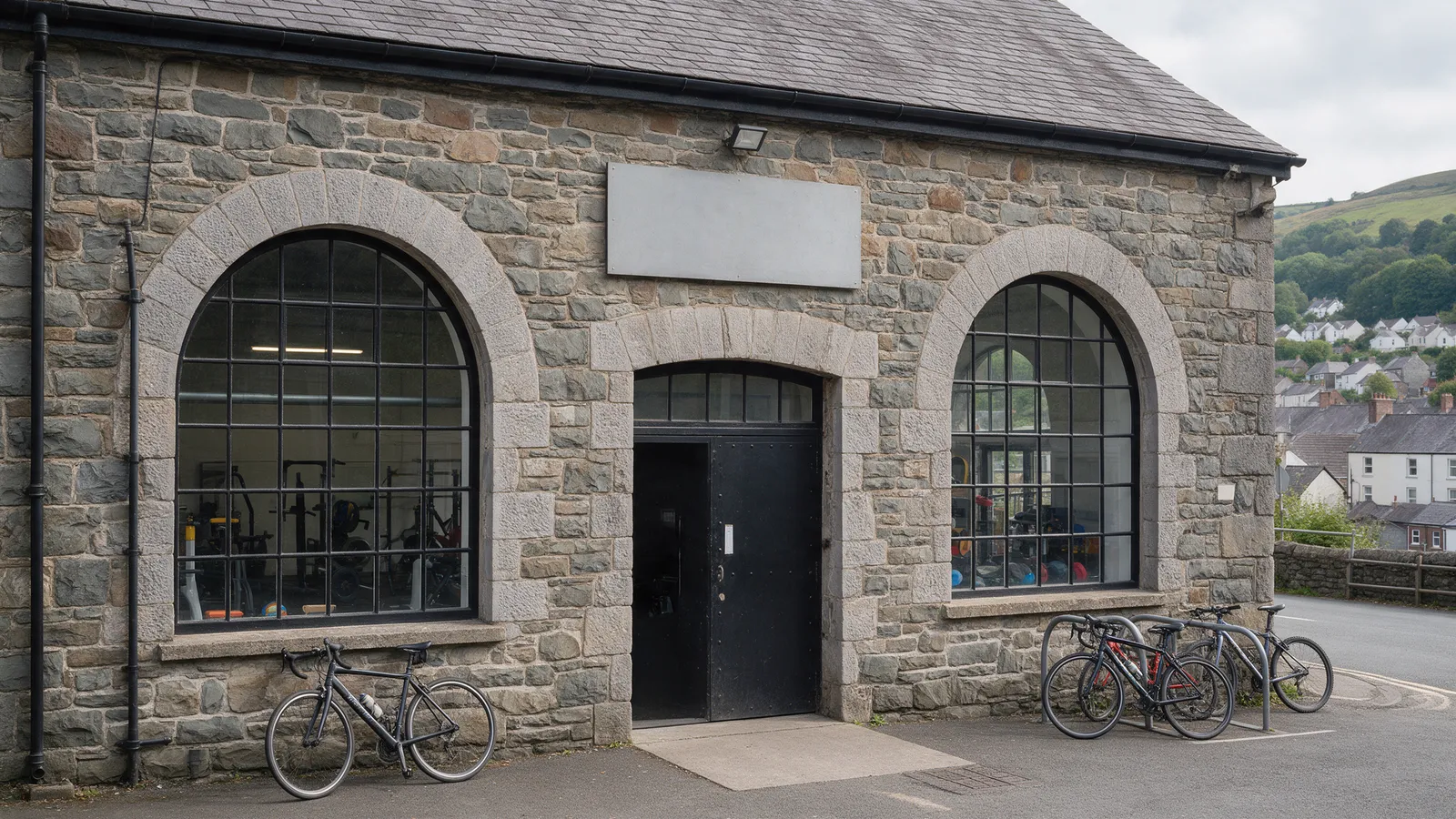 A converted stone warehouse gym exterior in a Welsh valley town with large arched windows, a black steel door and bikes outside
