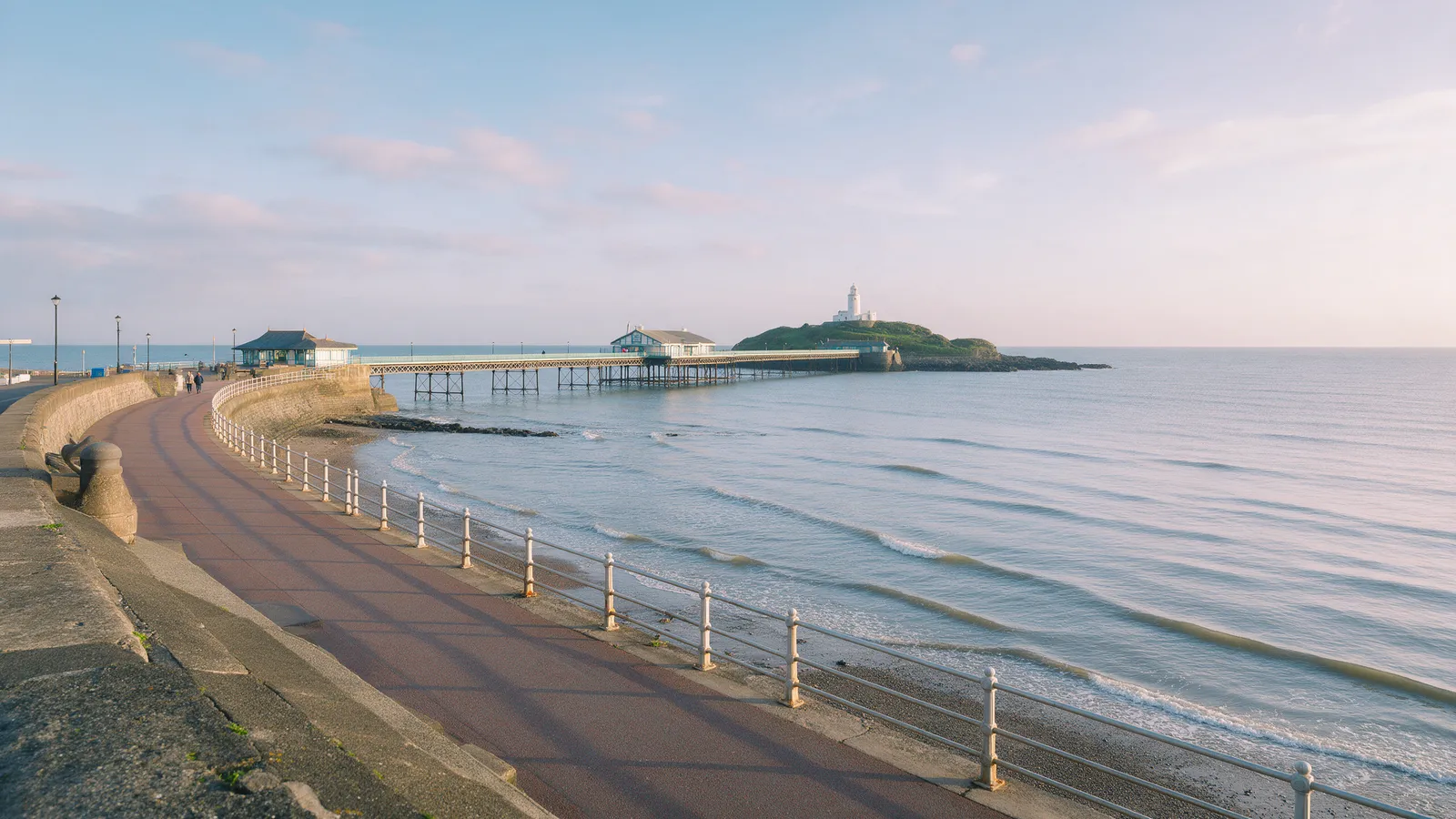 Mumbles seafront on a calm morning, the pier and the lighthouse in the distance, the promenade curving round the bay