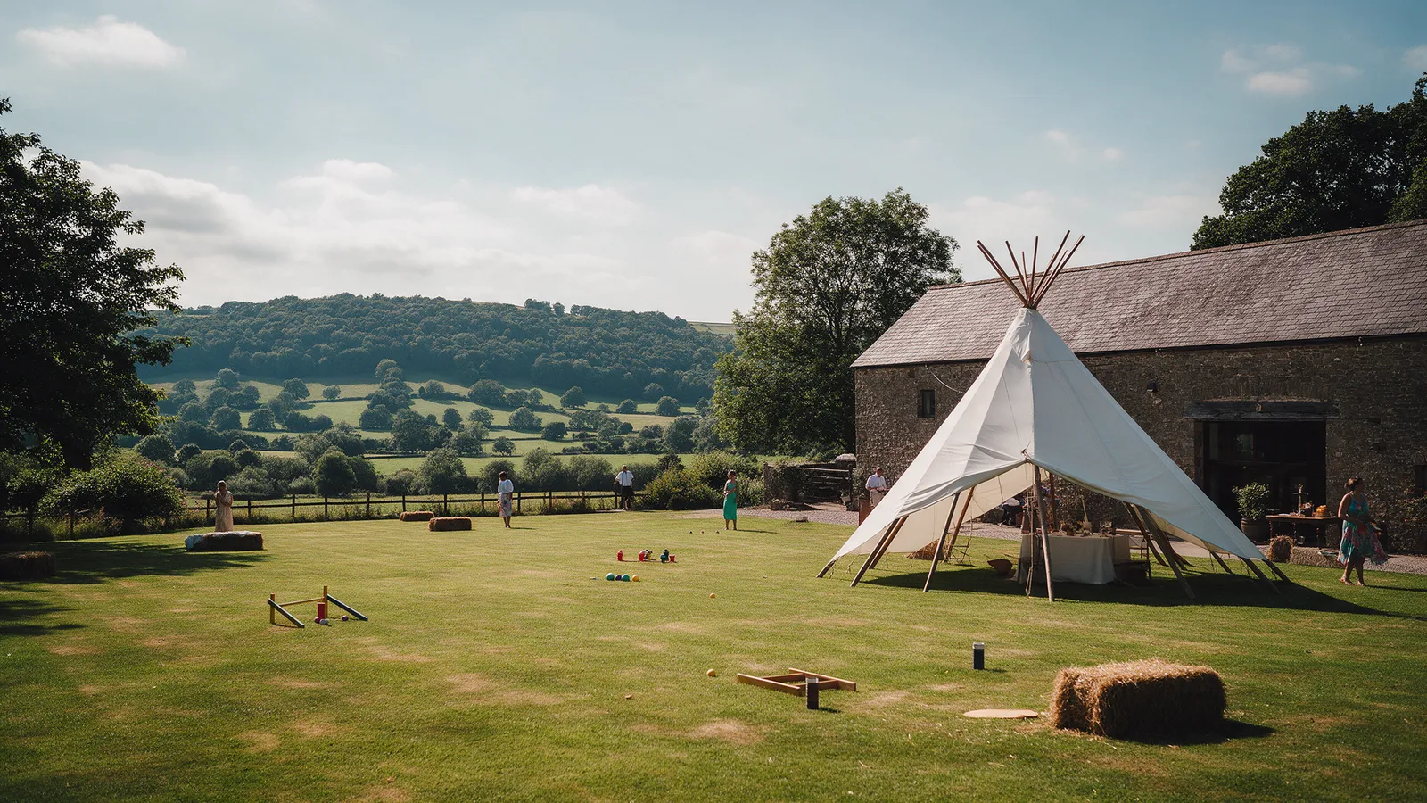 The Meadow beside the Barn with a sailcloth tipi, hay bales and lawn games and the Usk valley beyond
