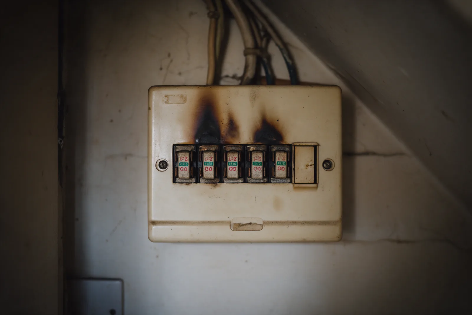 An old cream fuse box with rewirable fuses and scorch marks under the stairs